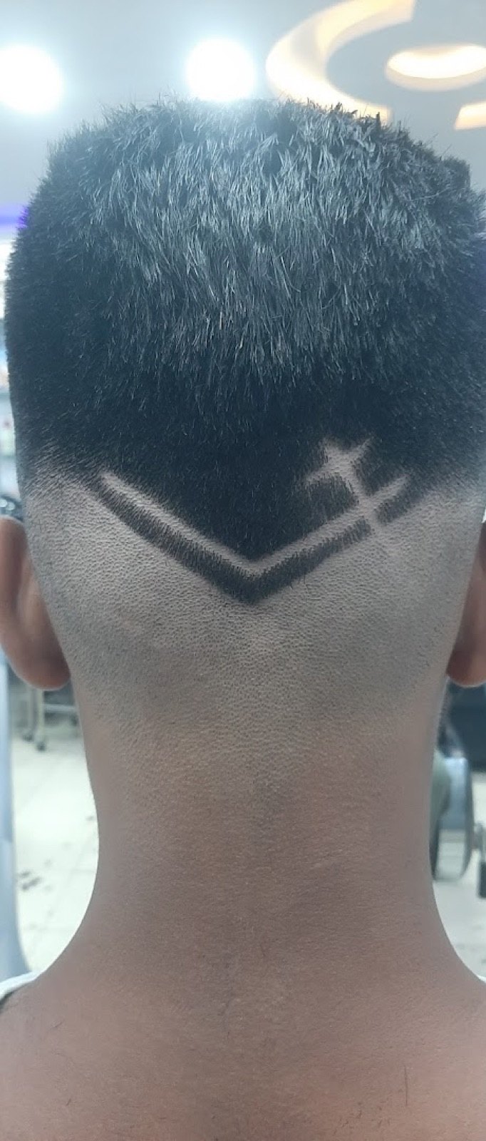 A skin fade with a razored chevron and arrow hair-tattoo design cut into the back of the head.
